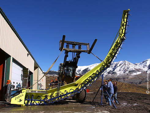 Setting Up for Pipe Cutter Prep : : : : : : : :
Thursday’s shot is of the vehicle maintenance crew maneuvering Crested Butte Mountain Resort’s Zaugg super pipe cutter into position for some preseason maintenance. I bet there are plenty of small parts to tighten and lube on that unit. The Zaugg and other cutters like it have always reminded me more of farm implements gone awry than snow shaping machines, but these are common equipment at ski resorts these days. While most of the super pipe shape is dozed into place by the cat crew, the final curve of the pipe is achieved by attaching this unit to the front of a snow cat and very carefully working it up and down the pipe. Operating the Zaugg no doubt takes a steady hand and an eye for detail!
: : : : : : : : Wednesday was mostly cloudy with snow showers in the high country around Crested Butte. Looks like we’re in for clearing and a bit of a warming trend as we head into the weekend, though. Have a great day and we’ll catch you tomorrow.